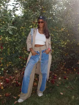 Tatiana Elizabeth wearing a trench coat, jeans, baseball cap and sneakers.