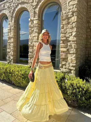 Woman wearing a baseball cap, a white tank top, and a yellow maxi skirt
