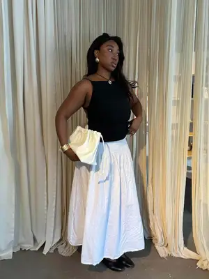 Nnenna Echem is wearing a black boatneck top, a white skirt, black mary janes, and holding a white handbag
