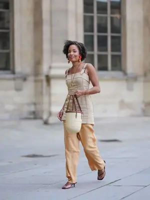 Ellie Delphine wears orange starfish / shell shaped earrings from Julietta, a beige linen tunic with shoulder straps from Mango, beige linen flowing pants from Mango, a basket raffia bag from Hunting Season, and heeled flip flops from Zara