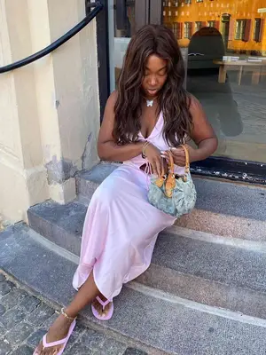 Nnenna Echem wears a pale pink dress, pink flip-flops, a butterfly necklace, and a blue handbag