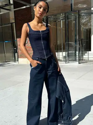 Yara Shahidi wears a dark blue denim corset, baggy jeans, and holds jean jacket