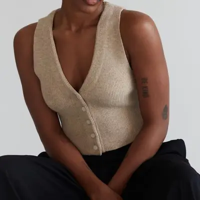 Close-up of model wearing Re Ona Knit Button Vest in beige paired with black pants