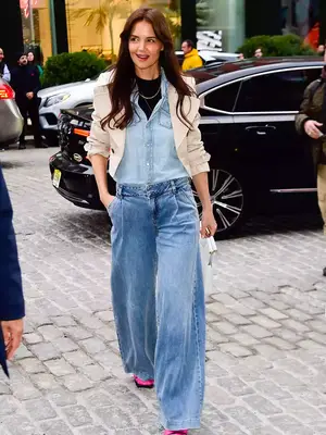 Katie Holmes wears a chambray button-down shirt, black top, paneled jeans, white blazer, necklaces, and white handbag