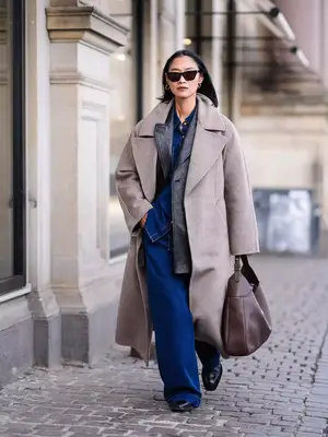 Woman wearing leather jacket, denim shirt and wide leg jeans, oversized coat, and brown leather bag