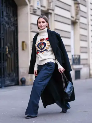 Woman wearing turtleneck sweater, wide leg jeans, longline black coat, and Chanel handbag