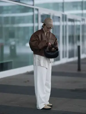 Woman wearing brown leather jacket, striped top, ecru wide leg jeans, tan boots, and tan Celine hat