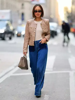 Woman wears structured beige jacket, white shirt, wide leg jeans, tan handbag, and sunglasses