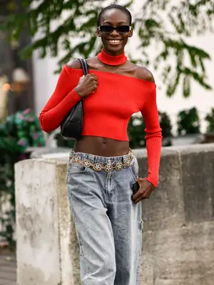 Woman wearing a two-piece red sweater, jeans, black shoulder bag, and sunglasses