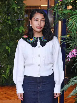 Woman wearing white sweater with crocheted collar and pearl-adorned buttons