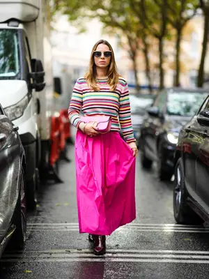 Woman wearing striped sweater, pink maxi skirt, boots, Valentino handbag, and sunglasses