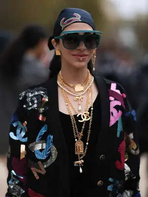 Woman wearing black top, Chanel sweater, gold layered jewelry, shield sunglasses, and headscarf