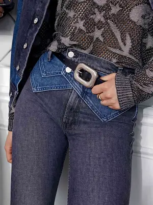 Close-up of person wearing textured open knit sweater and layered two-tone jeans and denim jacket