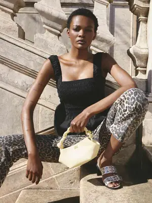 Woman wearing black top, leopard print jeans, silver two-strap heeled sandals, and butter yellow handbag