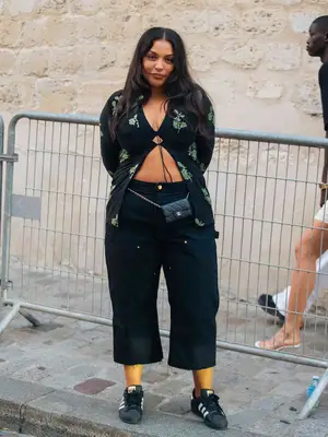 Paloma Elsesser wears a black and green tie front top, black wide leg pants, Chanel belt bag, and Adidas sneakers