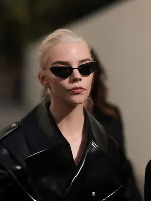 Anya Taylor-Joy wears black cat-eye sunglasses and a leather jacket