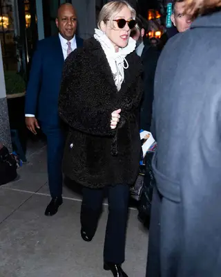 Chloe Sevigny wearing a faux fur coat with a white sweatshirt, sunglasses, black trousers, and black boots