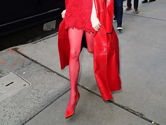 Close-up of Anya Taylor-Joy wearing red tights, shoes, minidress, and trench coat