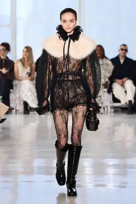 Model wearing sheer black lace outfit with fur collar and tall boots on Aknvas fall 2025 runway
