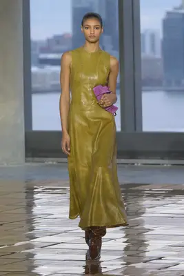 Model wearing green leather Ulla Johnson fall 2025 dress with purple handbag and brown boots