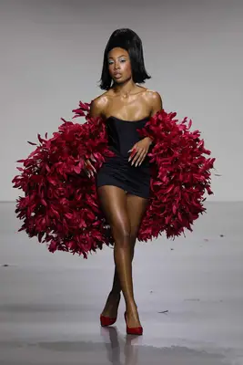 Model wears black corseted mini dress with voluminous red feathered wrap