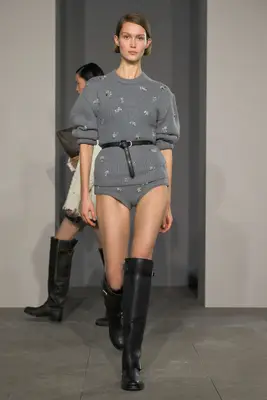 Model wearing gray knit sweater and hot pants with black tall boots on the Simkhai fall 2025 runway