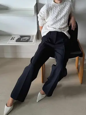 Close-up of person wearing cable knit sweater, dark trousers, and pointed-toe shoes