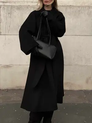 Woman carrying black handbag and wearing longline coat and leather gloves