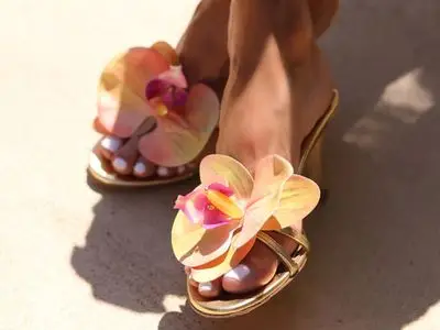 Feet wearing gold sandals with decorative yellow and pink floral designs