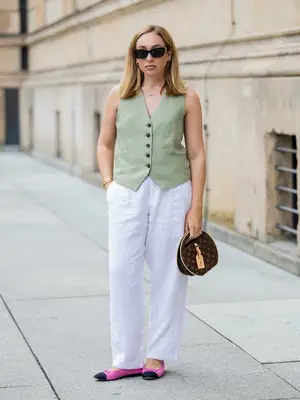 Sonia Lyson wears pink and black Chanel flats, white linen pants, light green Zara vest, Louis Vuitton bag, and Miu Miu sunglasses