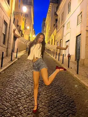 Olivia Rodrigo wearing a white blouse, denim shorts, and red Mary Jane heeled shoes