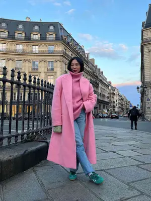Aimee Song wearing a pink turtleneck sweater with a long pink wool coat, light wash jeans, and green Adidas Sambas