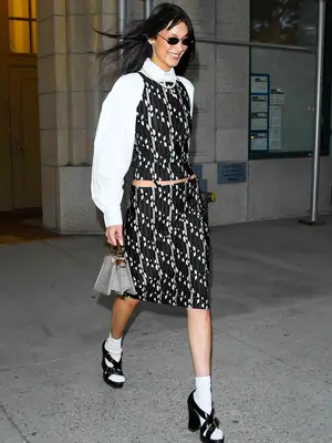 Bella Hadid wears a black and white top and skirt set, white blouse, tiny sunglasses, and platform heels
