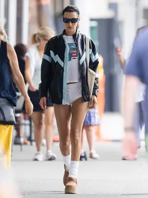 Bella Hadid wears a Lego T-shirt, white boxers, a long leather jacket, Uggs, and a tote bag