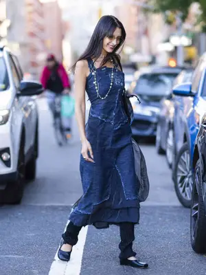 Bella Hadid wears a denim maxi dress, knit leg warmers, flats, Chanel pearls, and transparent sunglasses