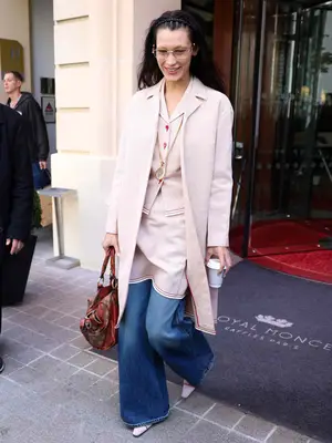 Bella Hadid wears a tailored blazer, pants, and oversized coat set with glasses and a Louis Vuitton bag