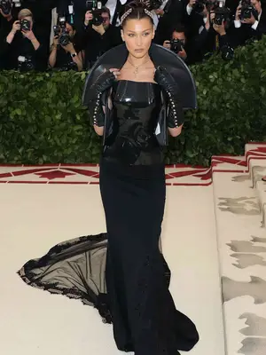 Bella Hadid wears a black Chrome Hearts gown with sheer train, patent leather top, and fingerless gloves to the 2018 Met Gala