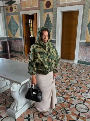 Paloma Elsesser wears a pixellated camo windbreaker jacket, linen maxi skirt, barefoot shoes, and black handbag