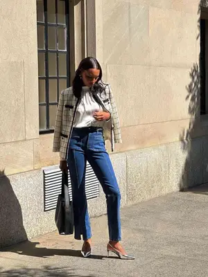 Jasmine Tookes wears a black and white boucle jacket, seamed denim, white top, silver heels, and black tote