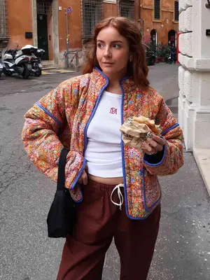 Woman wears colorful quilted jacket, white ribbed tank top, and burgundy drawstring sweatpants