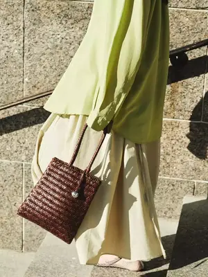 Person carrying a woven bag walking by a textured wall