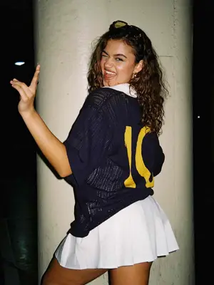 Madison Bailey wearing a navy loose knit top with the number 10 and a white pleated skirt
