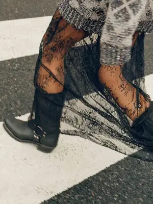 Close-up of person wearing sweater, sheer lace skirt and tights, and motorcycle boots