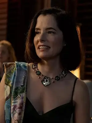 Parker Posey wears an enamel shield necklace, black dress, and colorful patterned shawl on The White Lotus season 3