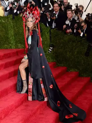 Sarah Jessica Parker at the Met Gala wearing a black gown and a red headpiece