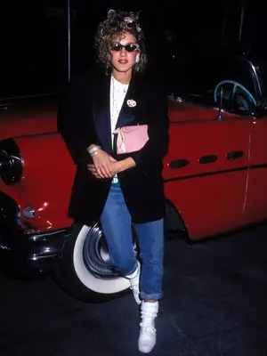 Sarah Jessica Parker wearing an oversized blazer with jeans, white sneakers, and a pink purse