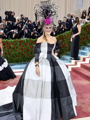 Sarah Jessica Parker at the Met Gala wearing a black-and-white plaid ball gown with a floral and feathered fascinator headpiece