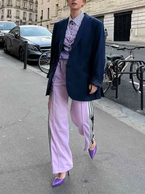 person wearing a navy blazer, lilac track pants, a lavender button-down shirt, and purple heels. 
