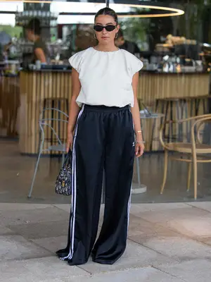 Person wearing sunglasses, a bubble top, black track pants, and bracelets. They