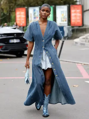 Woman wearing denim button-front maxi dress over striped skirt, blue metallic cowboy boots, and baby blue mini handbag